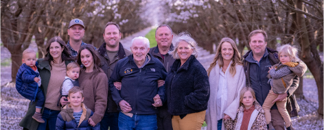 Three-generation farming family standing in an almond orchard, consisting of husbands, wives, grandparents, grandchildren, and a great grandpa.
